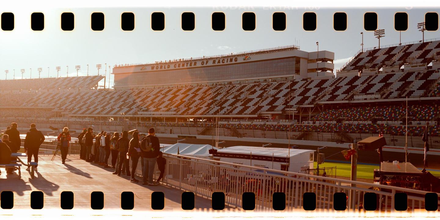A crowd of people stands on a walkway overlooking a large stadium with empty seats and a building labeled "World Center of Racing" in the background.