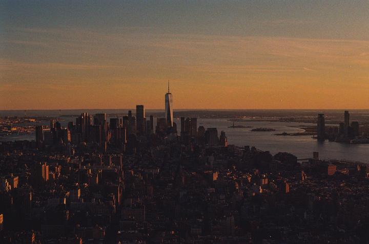 An aerial view of the New York City skyline at sunset shows the One World Trade Center building towering over other structures.