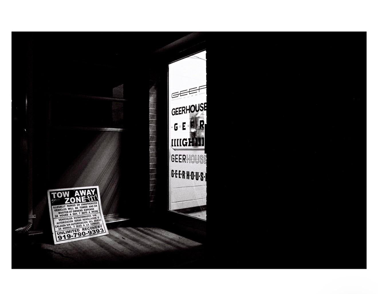 A "Tow Away Zone" sign sits on the ground next to a building with a window displaying the word "Geerhouse" in black and white.