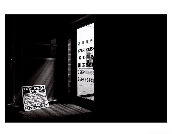 A "Tow Away Zone" sign sits on the ground next to a building with a window displaying the word "Geerhouse" in black and white.