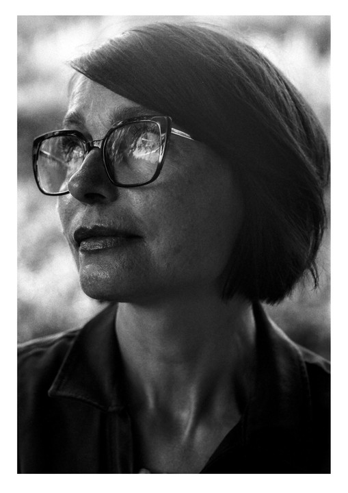 A woman with short hair and glasses looks to the side in a close-up portrait.