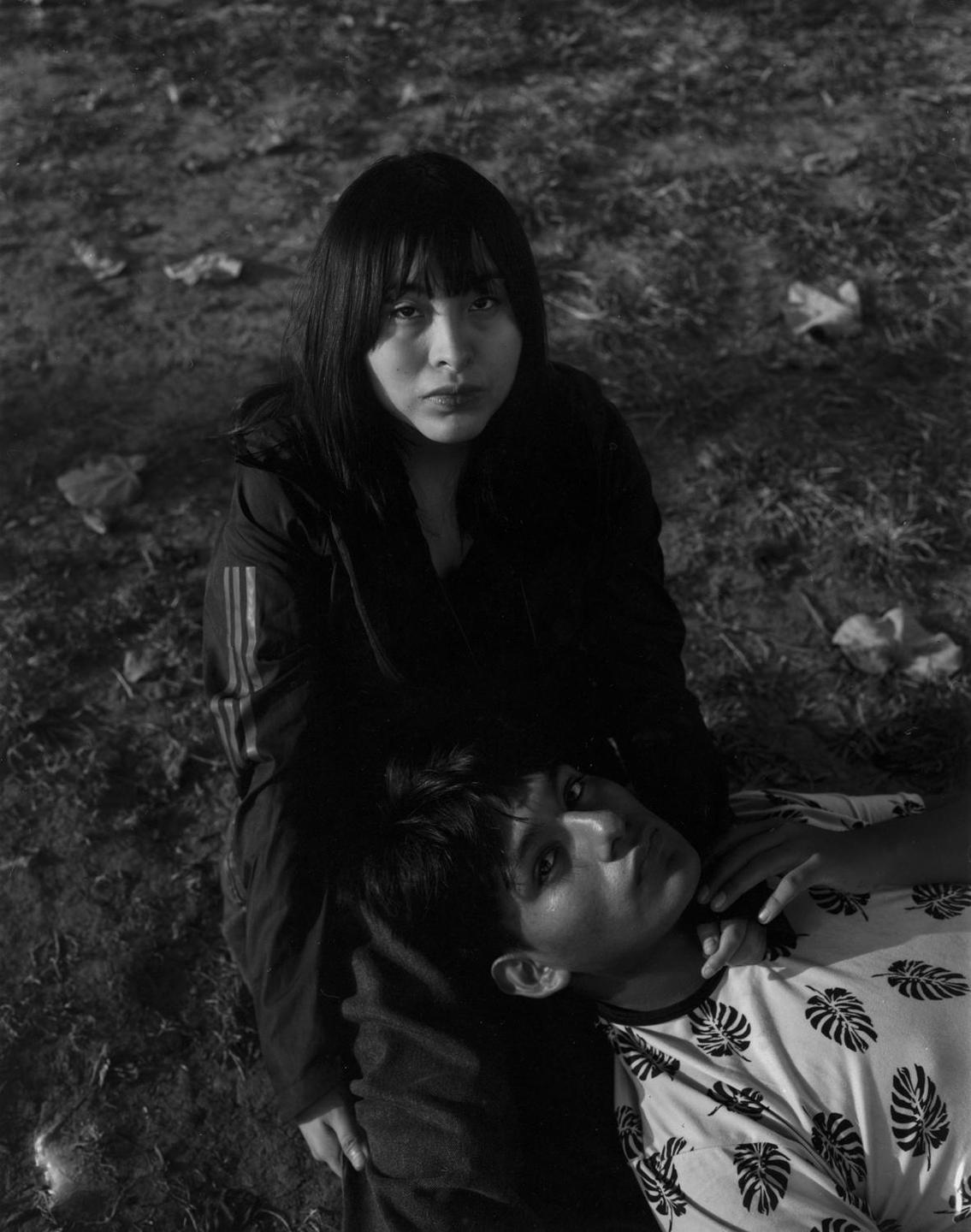 A woman sits with a man resting his head on her lap, both looking up at the viewer.