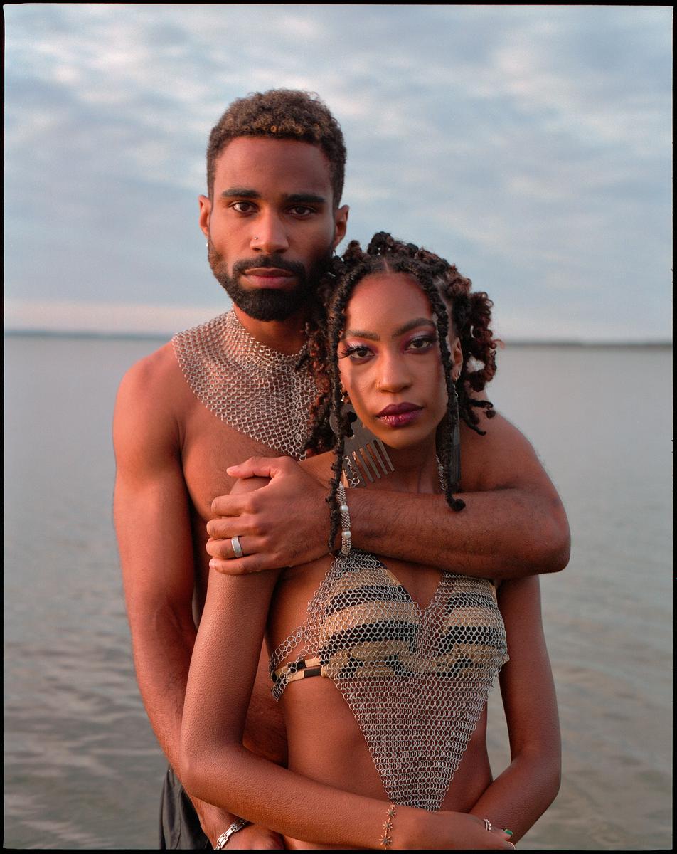 A man and a woman wearing chainmail stand in water with their arms around each other.