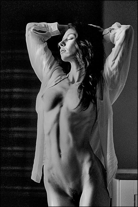 A woman with her eyes closed and arms raised is illuminated by strong light from the side.