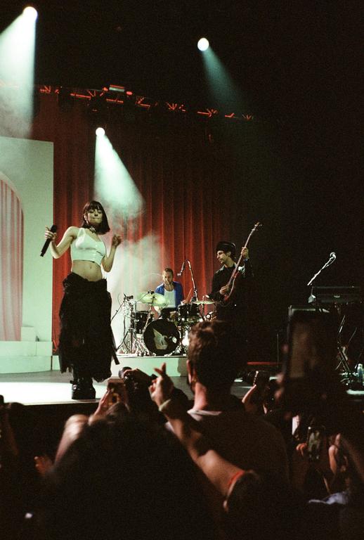 A woman sings into a microphone on stage with a band and an audience.