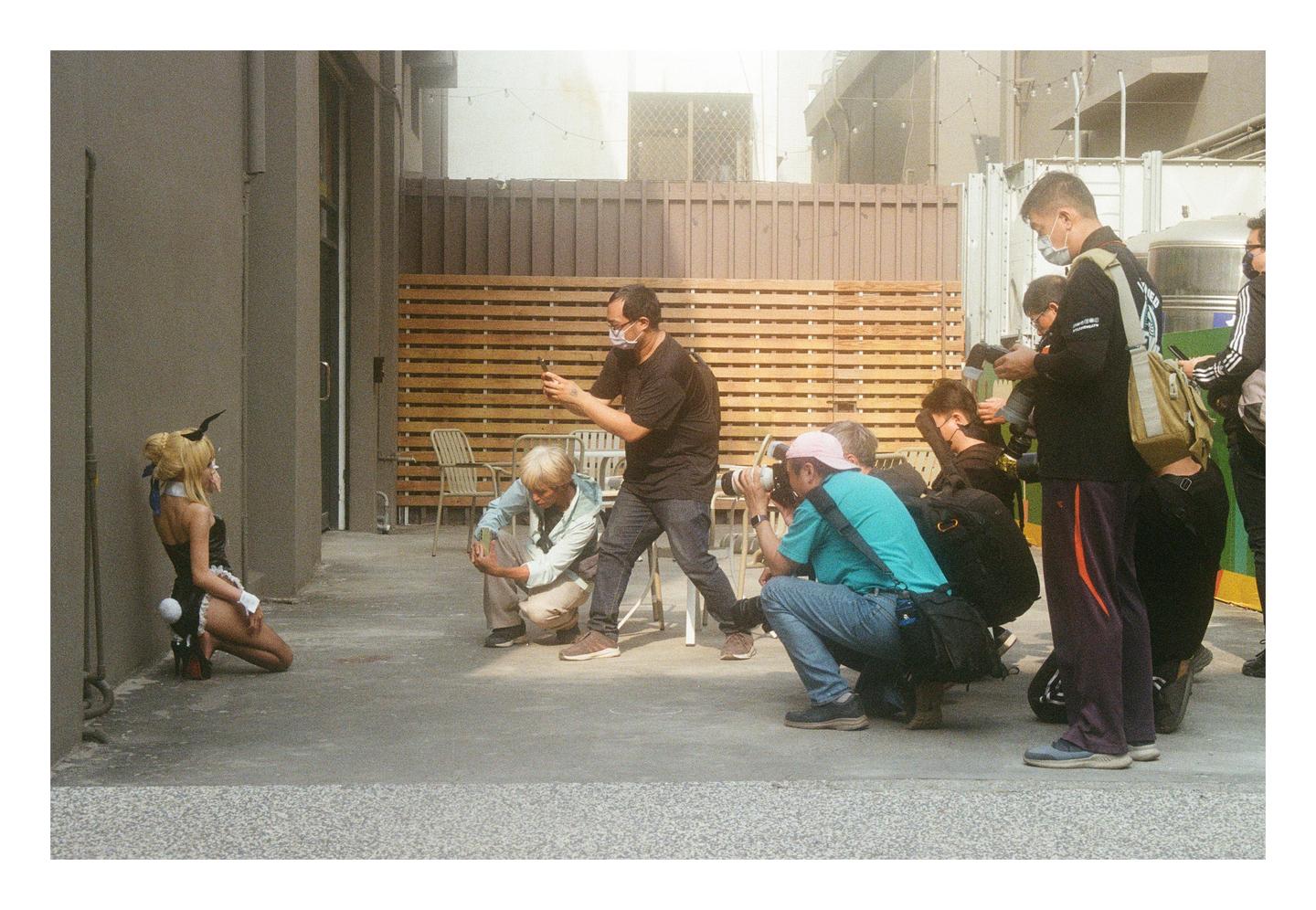 A group of photographers are taking pictures of a woman in a bunny costume kneeling on the ground.