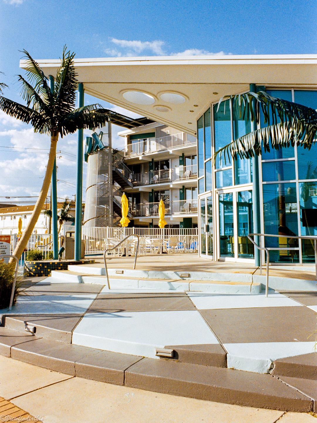A modern building with blue glass windows and palm trees stands under a clear sky.