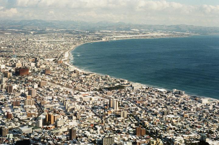 An aerial view shows a snow-covered city along a curved coastline next to a large body of water.