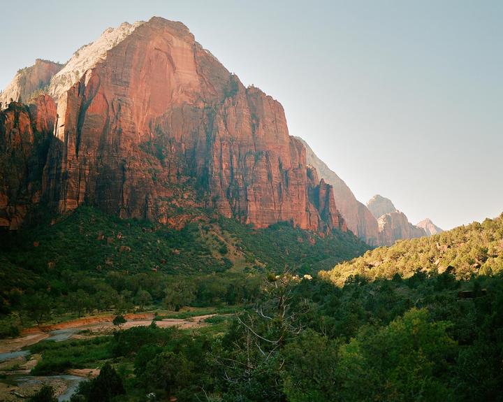 A large red mountain rises above a green valley with a river.