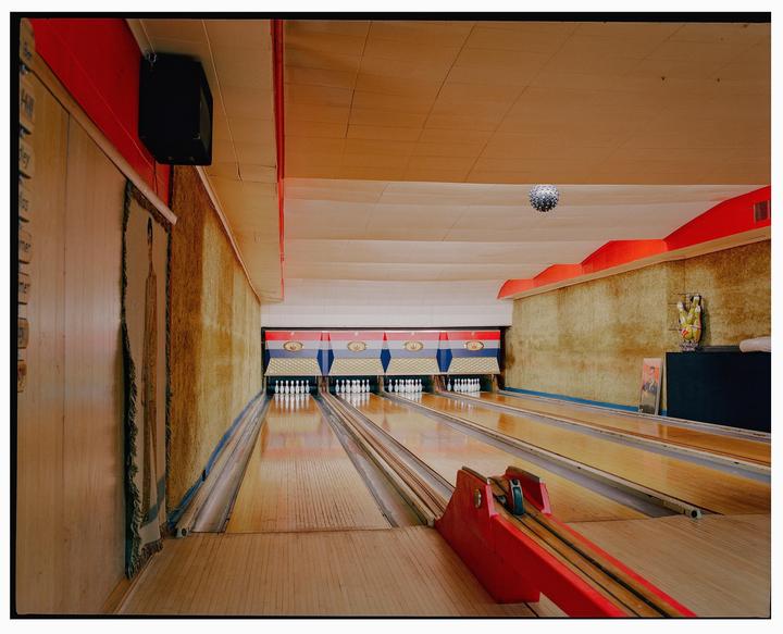 A bowling alley with three lanes and a disco ball hanging from the ceiling is visible from the perspective of the bowler.