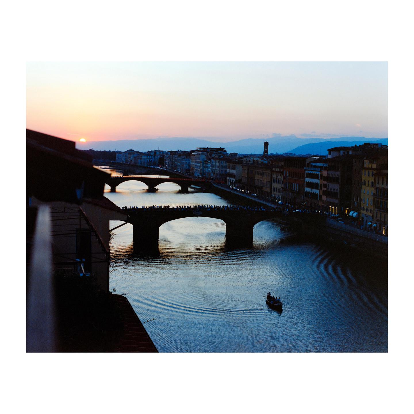 A river with several bridges and buildings along its banks is visible at sunset.