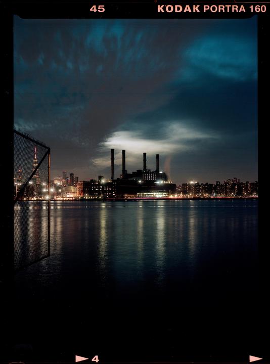 A city skyline with a power plant and its reflection on the water at night.