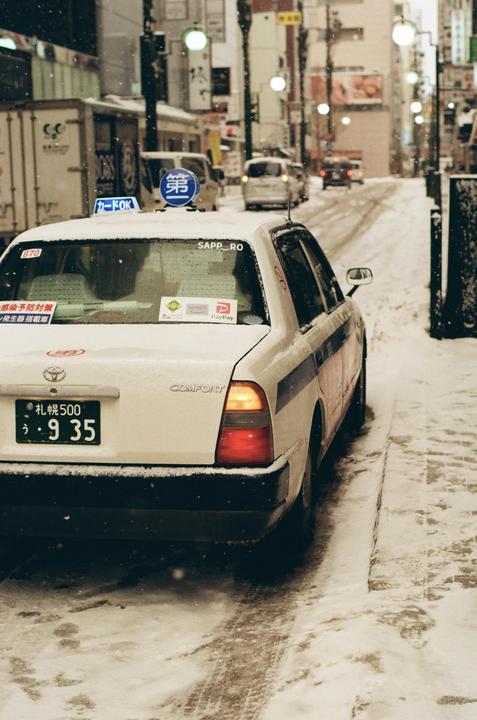 A white taxi is parked on a snow-covered street in a city.