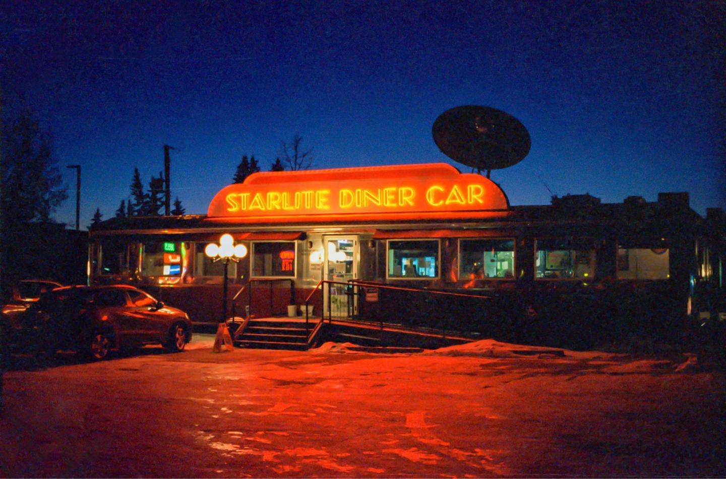 A diner with a neon sign that reads "Starlite Diner Car" is illuminated at night, with a car parked in front.