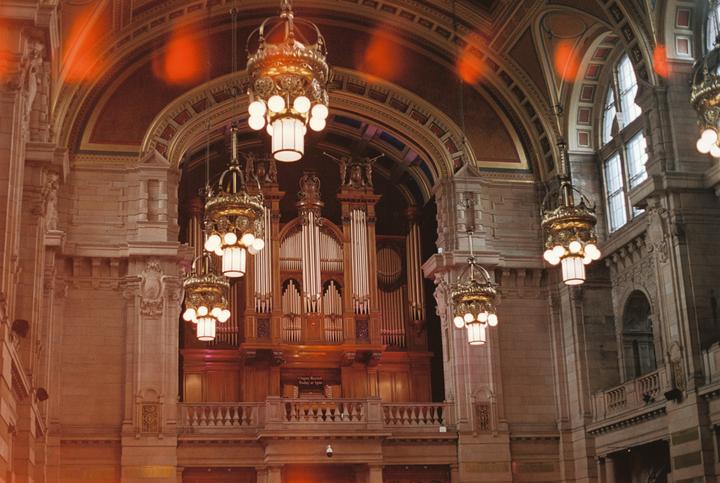 A large pipe organ is visible behind ornate chandeliers in a grand hall.