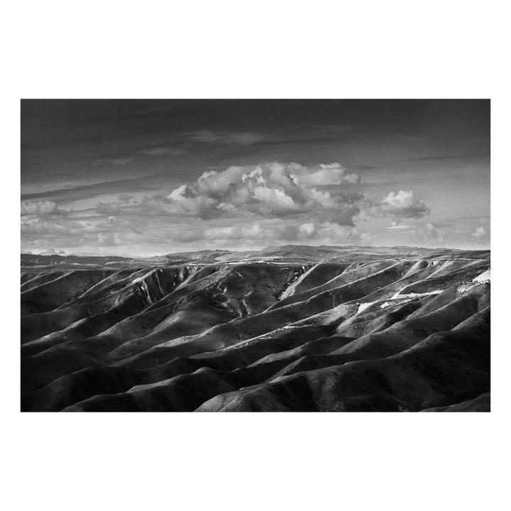 A black and white landscape shows rolling hills under a cloudy sky.