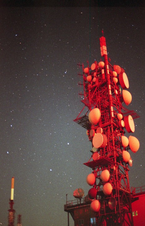 A red radio tower stands against a night sky filled with stars.