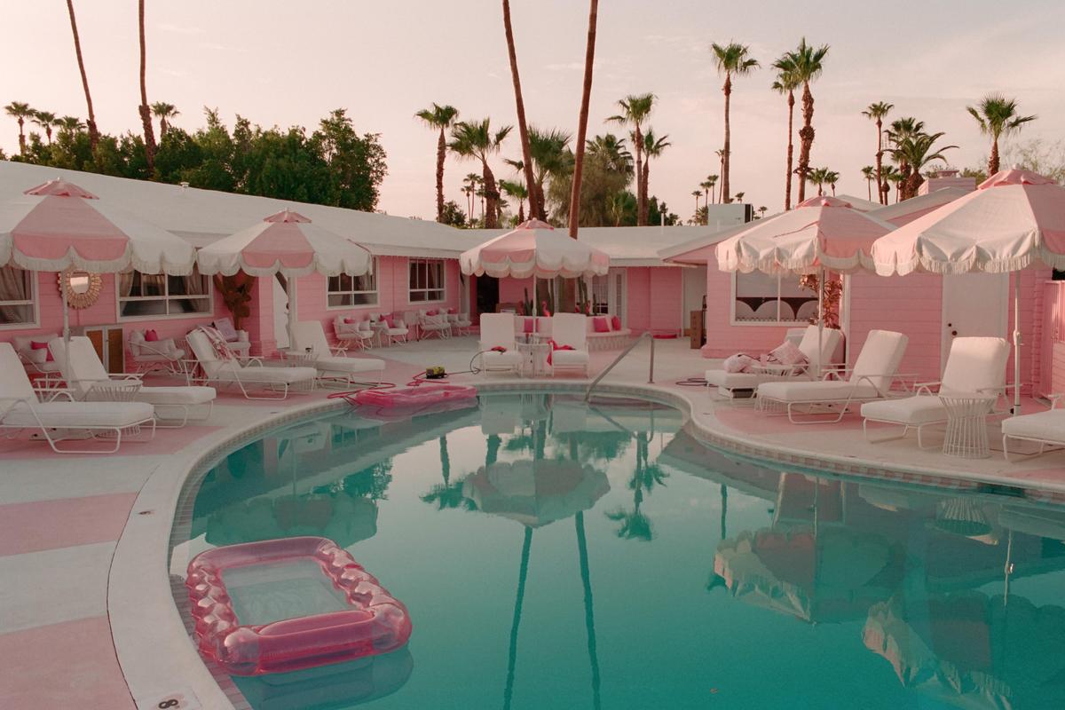 A pink motel with white umbrellas and lounge chairs surrounds a swimming pool with a pink inflatable raft.