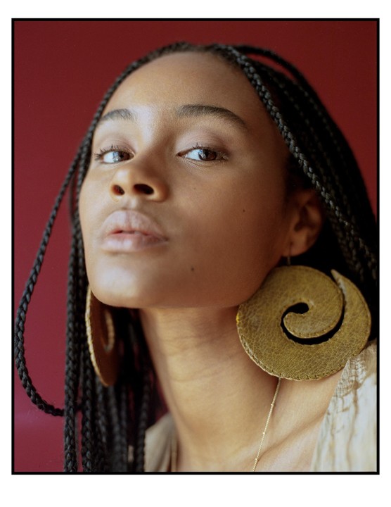 A woman with braided hair and large spiral earrings looks directly at the viewer.