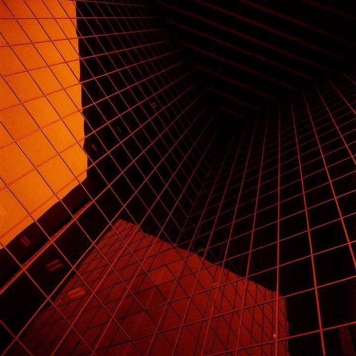 A low-angle view of a modern building with a grid pattern on its facade, reflecting an orange hue.