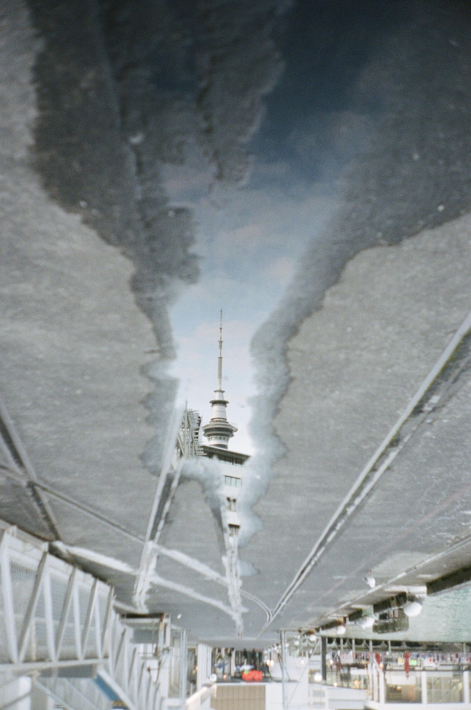A tall tower is reflected in a puddle on a concrete surface.