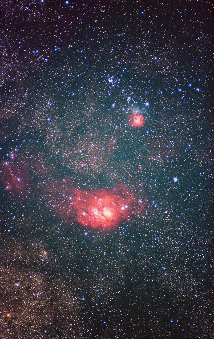 A vast expanse of stars and nebulae fills the frame, with two prominent red nebulae glowing brightly.