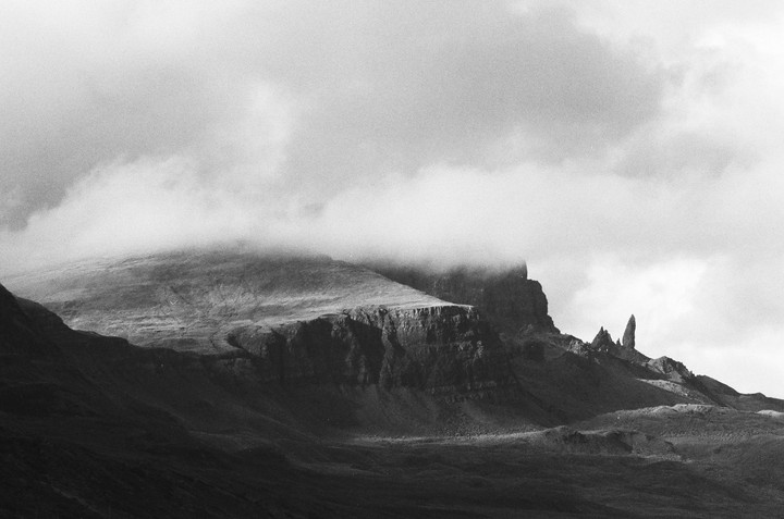 Clouds cover the top of a mountain range with a prominent rock formation on the Isle of Skye.