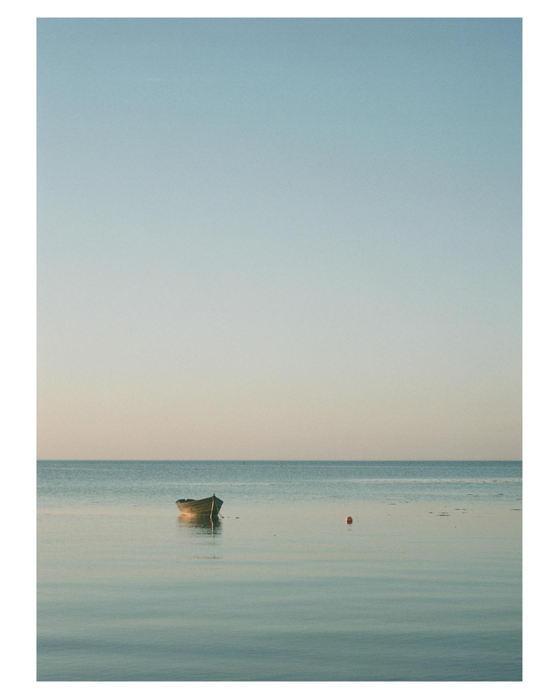 A small boat floats on calm water under a clear sky.