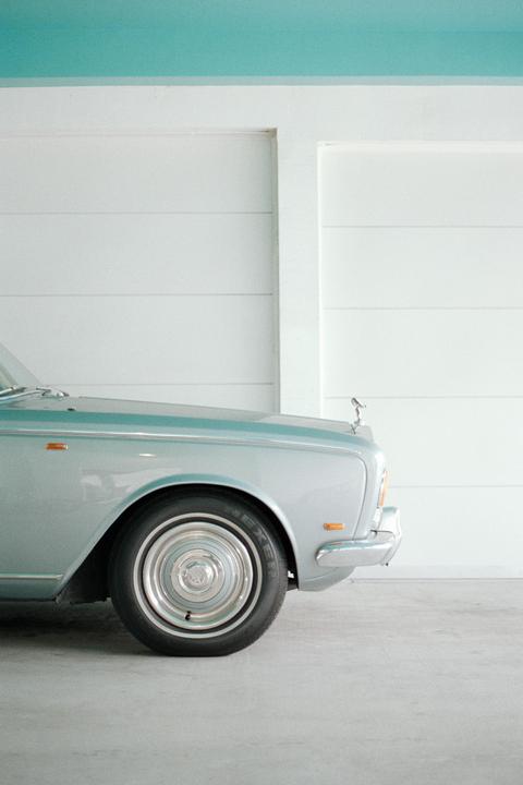 A silver vintage car is parked in front of a white wall with a blue ceiling.