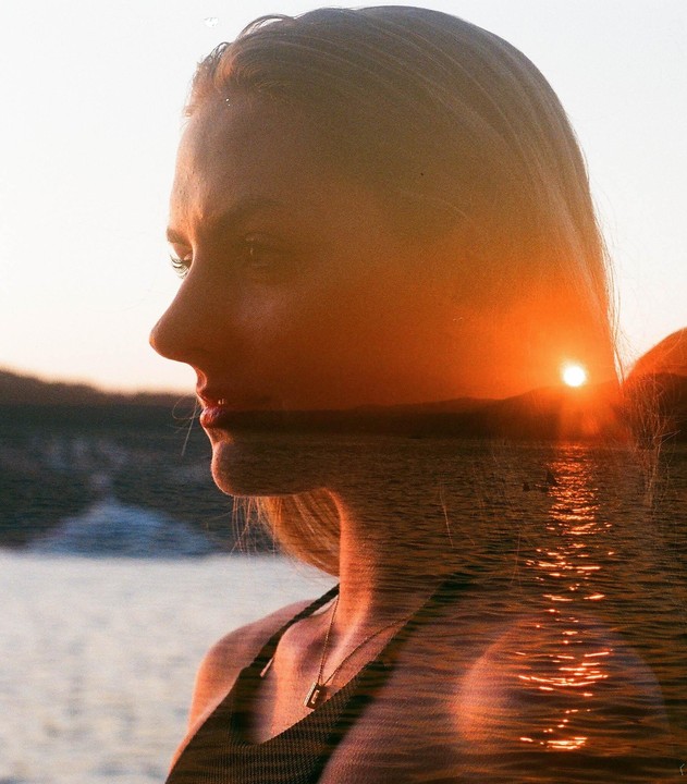 A double exposure shows a woman in profile overlaid with a sunset over water.