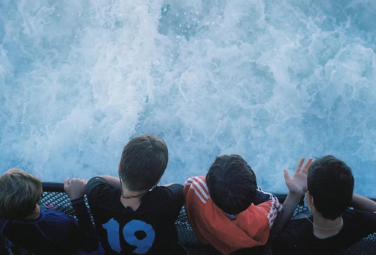 Four boys look down at the churning water from a boat.