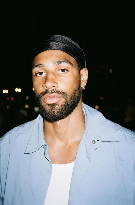 A man with a beard and a black durag looks directly at the viewer.