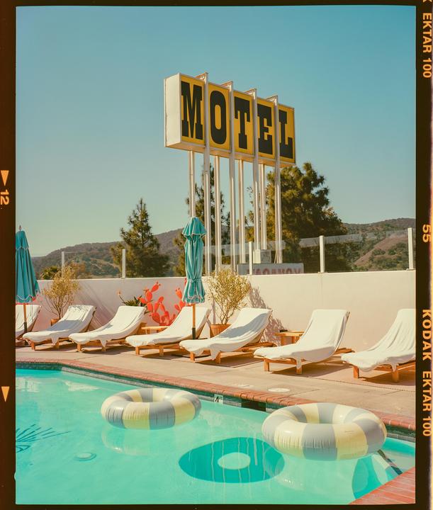 A motel sign stands above a swimming pool with lounge chairs and inflatable rings.