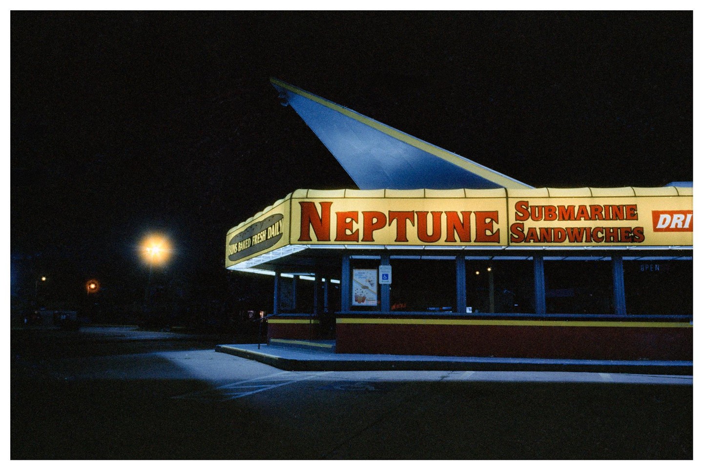A brightly lit Neptune Submarine Sandwiches restaurant stands out against the dark night sky.