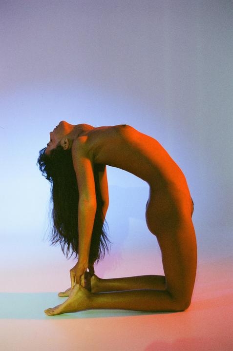 A woman with long hair is kneeling and bending backward in a yoga pose with colorful lighting.