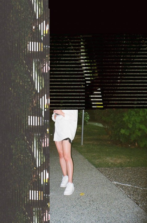 A woman stands on a sidewalk next to a grassy area, with vertical and horizontal stripes obscuring parts of the image.