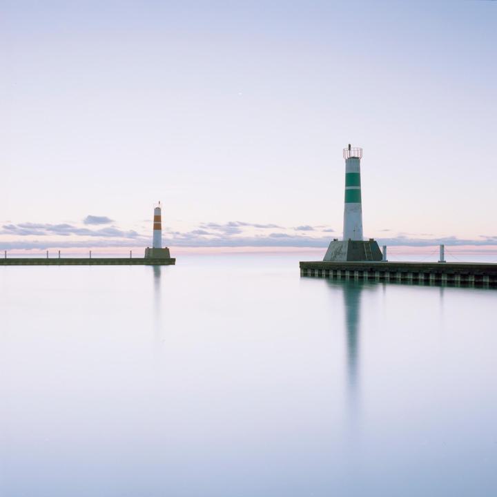Two lighthouses stand on piers extending into calm water under a pale sky with a few clouds.
