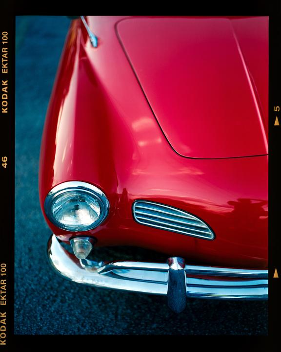 The front of a red vintage car with a chrome bumper and headlight is visible.
