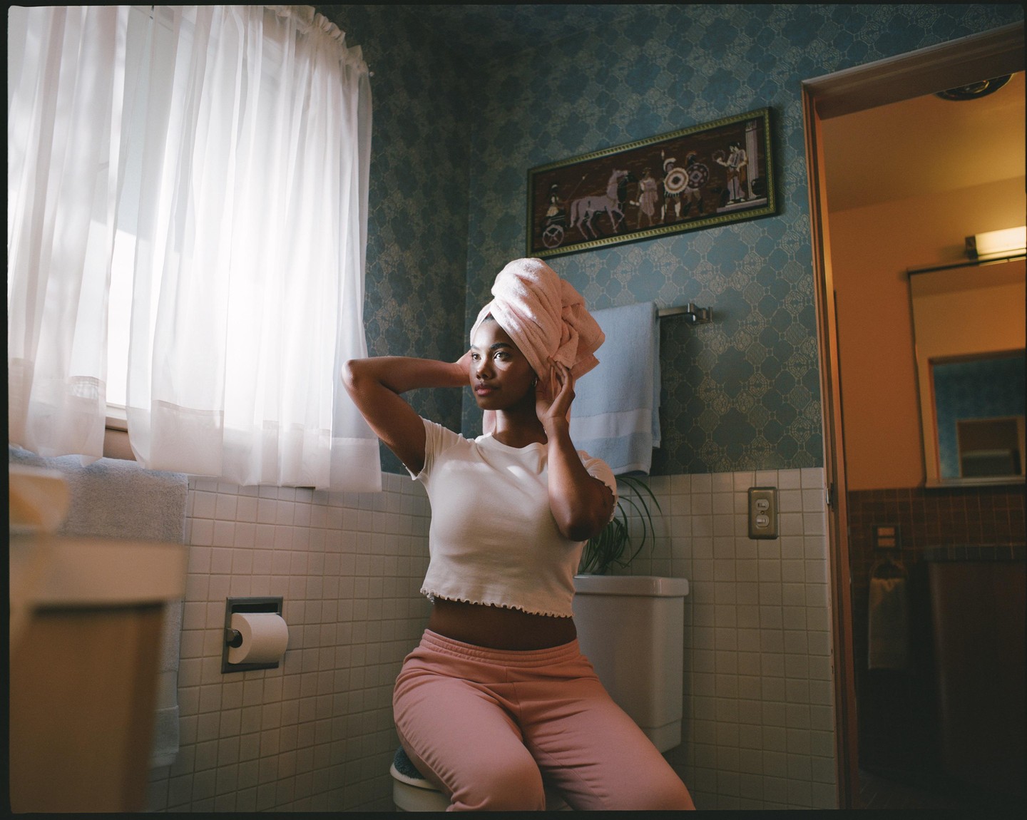A woman with a towel wrapped around her head sits in a bathroom.
