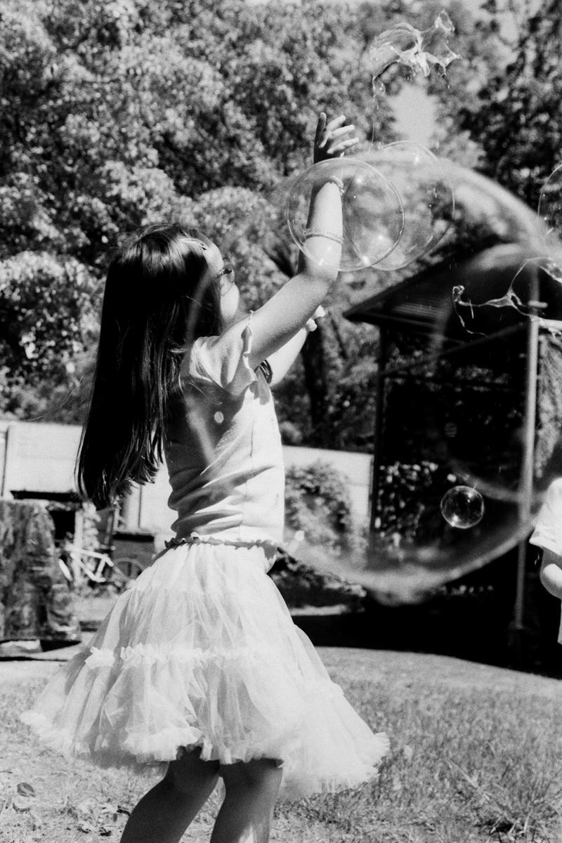 A girl in a ruffled skirt plays with bubbles in a garden.