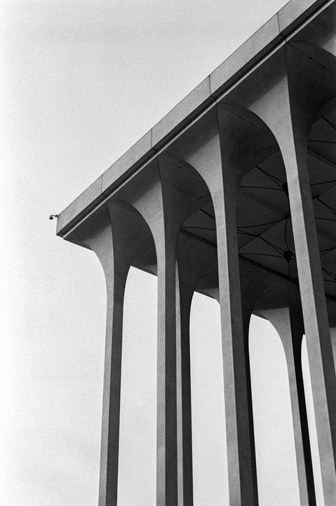 A low-angle view shows a series of concrete arches supporting a building, with a security camera visible on the far left.