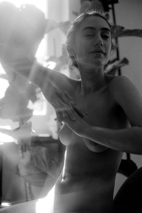 A woman with her arms raised is illuminated by bright light from the left.