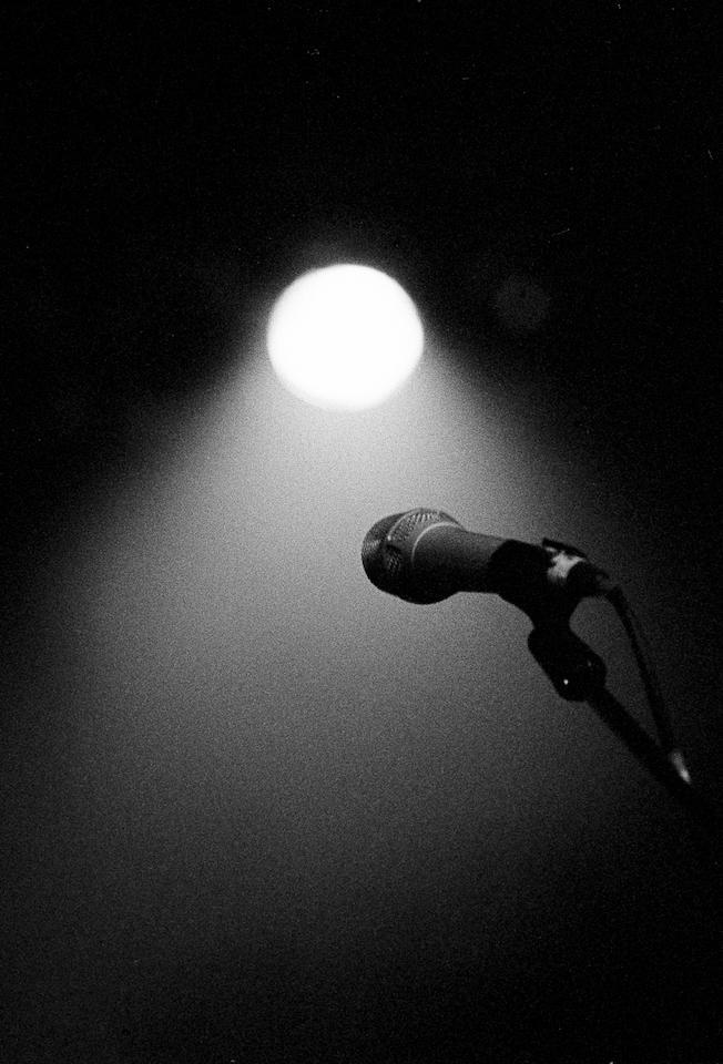 A microphone stands on a stage illuminated by a single spotlight.