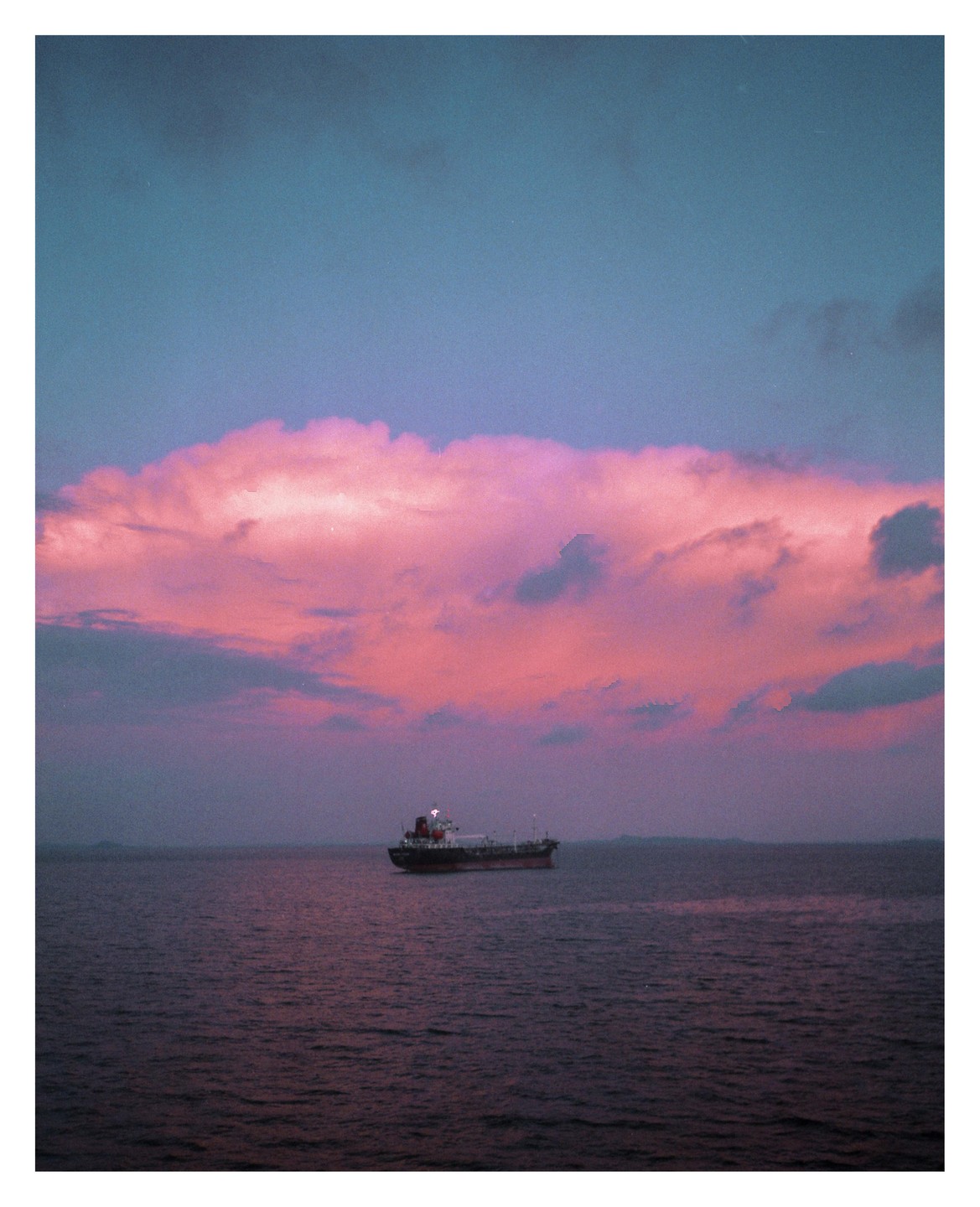 A ship floats on the water under a sky filled with pink clouds.
