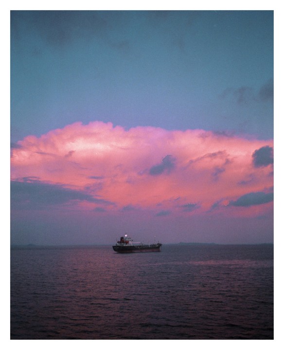 A ship floats on the water under a sky filled with pink clouds.