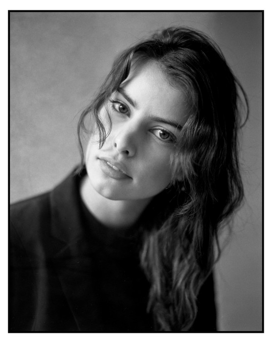 A woman with long, wavy hair looks directly at the viewer.