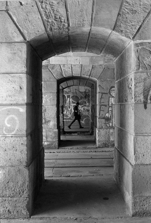 A person walks through a series of stone archways covered in graffiti.