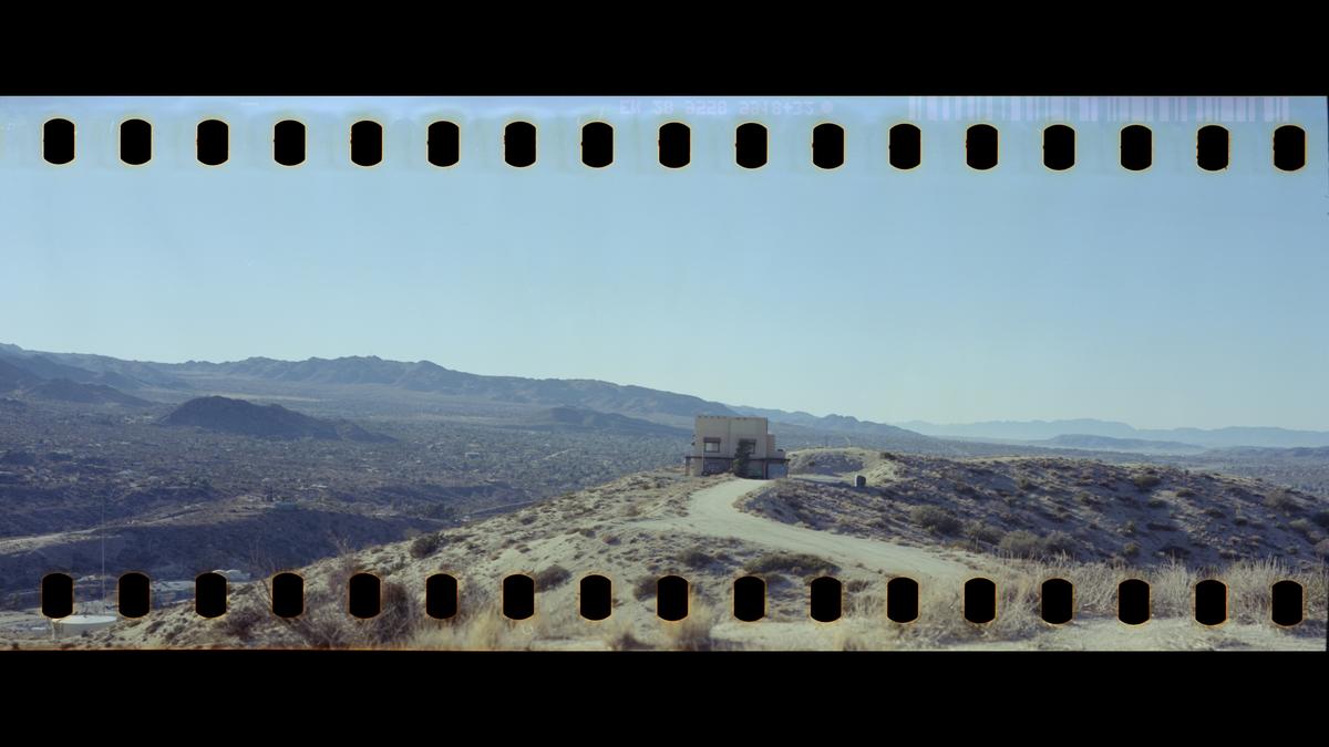 A building sits on a hill with a winding road leading to it, surrounded by a vast desert landscape under a clear sky.