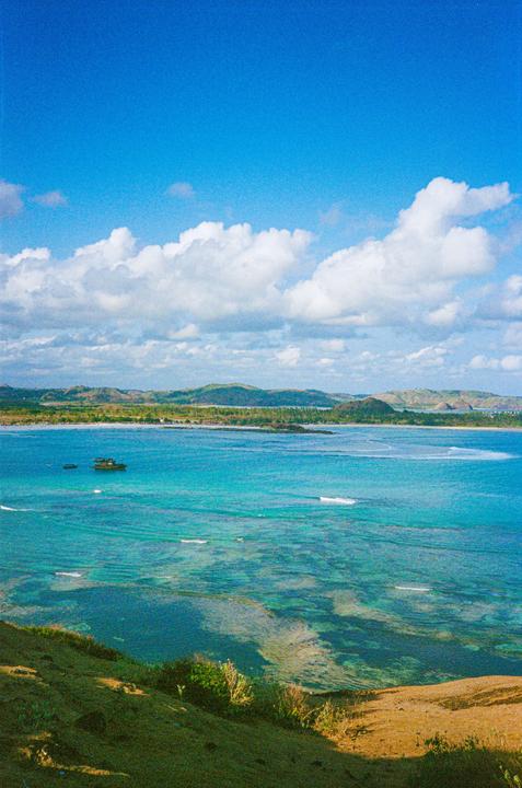 A boat floats on clear blue water with hills in the distance under a bright sky.