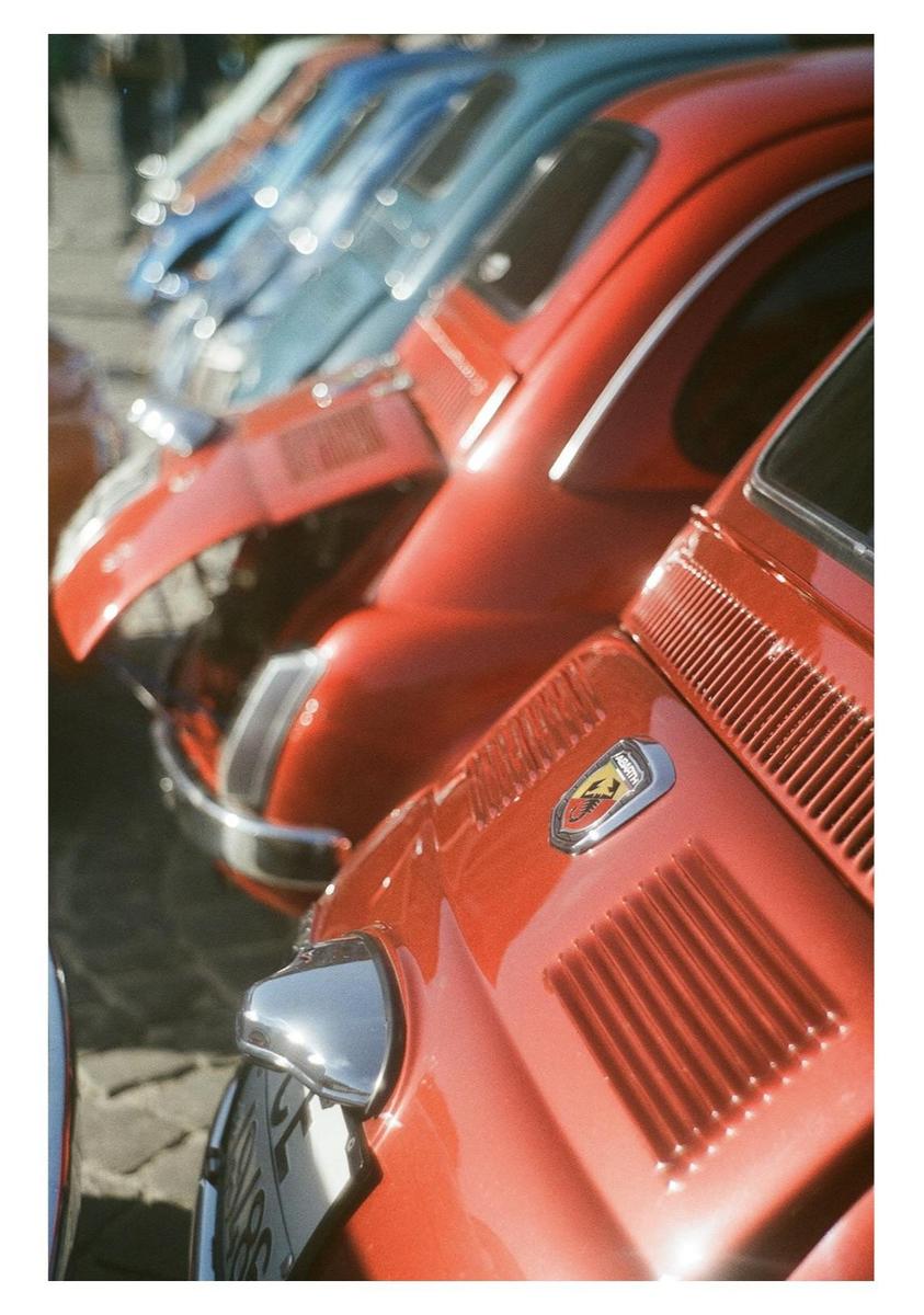 A line of red and blue Fiat cars are parked with their hoods open.
